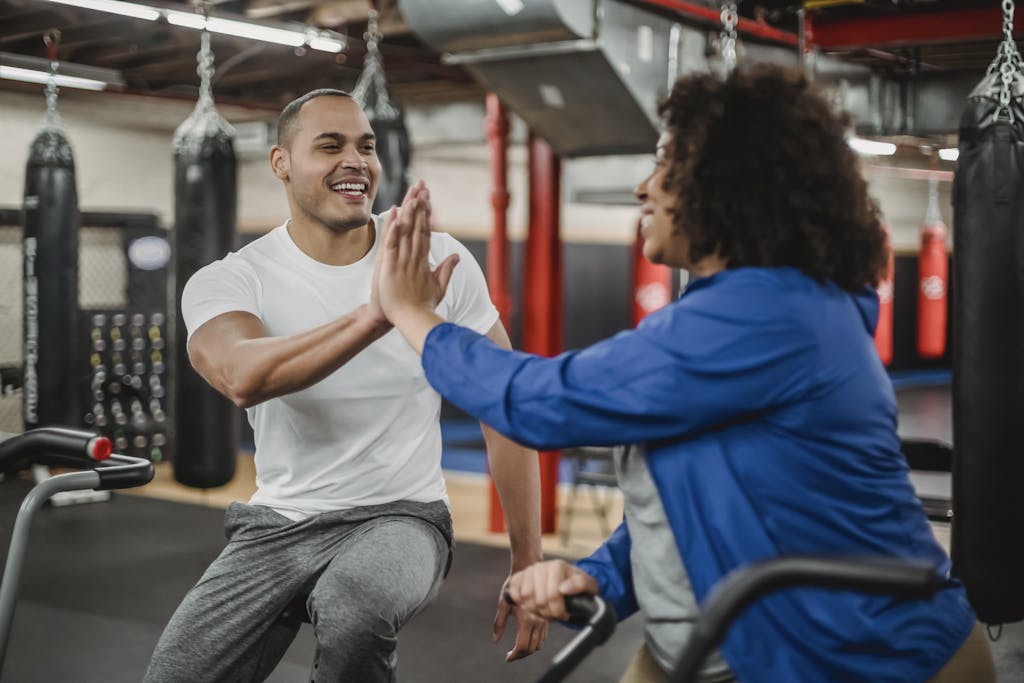 Cheerful plump black female trainee and smiling fit male instructor clapping each others hands in modern gym